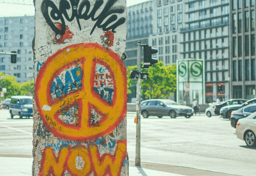Orangefarbenes Peace-Symbol als Graffiti auf einem Stück einer Mauer an einer Straßenkreuzung.