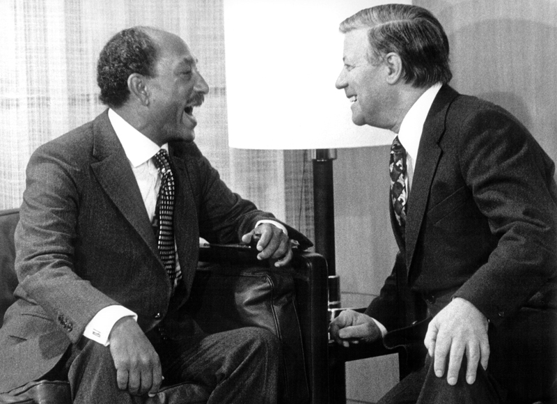 Anwar alSadat und Helmut Schmidt sitzen auf Ledersesseln und schauen sich an.