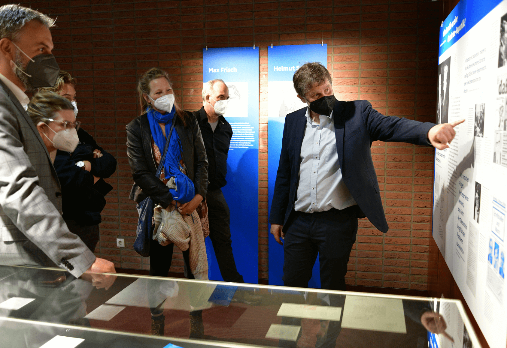 Magnus Koch zeigt Besucherinnen ein Bild auf einer Ausstellungstafel.