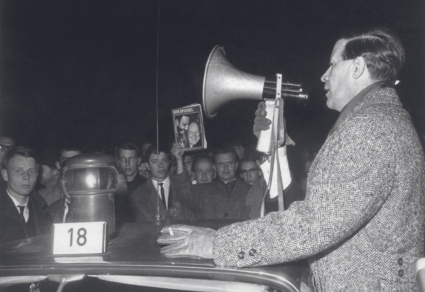 Helmut Schmidt spricht in ein Megafon. Im Hintergrund hält ein Mann eine Ausgabe des Magazins "Der Spiegel" hoch. 