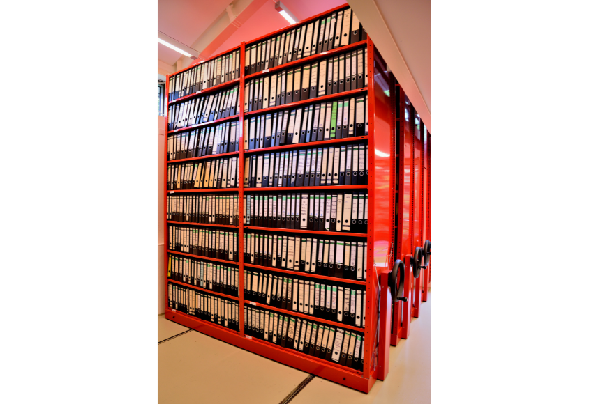 Blick ins Schmidt-Archiv. In roten Archivregalen stehen Aktenordner.