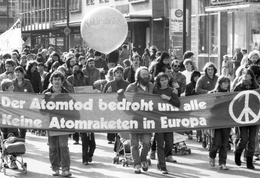Historisches Foto von Demonstrierenden. Auf einem großen Banner steht "Der Atomtod bedroht und alle - Keine Atomraketen in Europa"