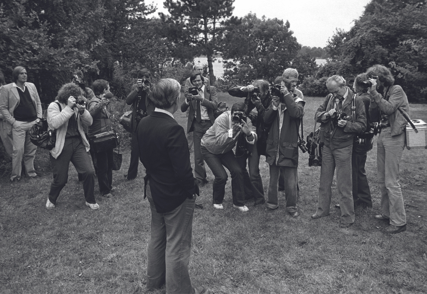 Etwa 15 Fotografen stehen in einem Halbkreis um Helmut Schmidt herum, der in die Kameras schaut. Man sieht Schmidt von hinten, die Fotografen von vorne