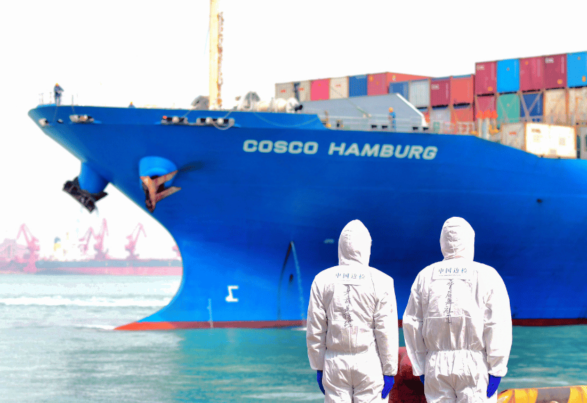 workers in protective suits stand near a COSCO container ship docked at a port in Qingdao in eastern China's Shandong Province.