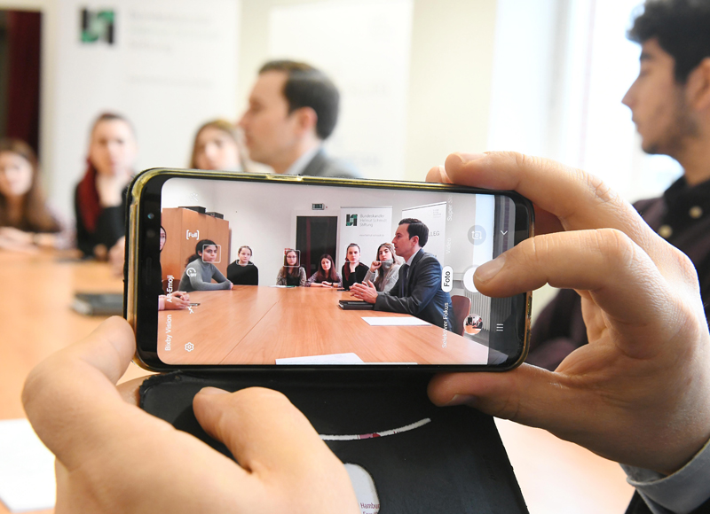 Blick durch eine Handykamera: Jemand macht ein Foto von einem Meeting. 