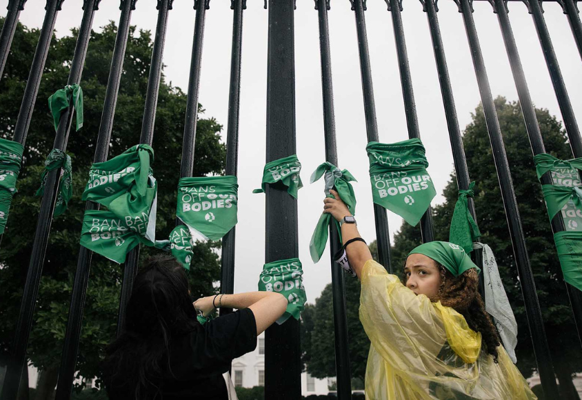 Als Protestaktion binden zwei Frauen bedruckte, grüne Tücher an einen hohen Zaun.