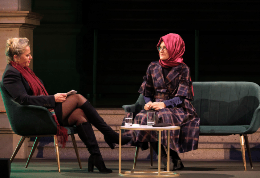 Susanne Koelbl in schwarzen Stiefeln und rotem Schal neben Hatice Cengiz in kariertem Kleid auf dem Podium.