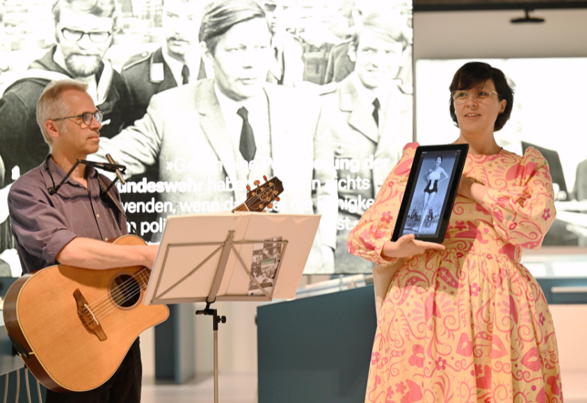Ein Musiker und eine Frau mit Tablett stehen in der Ausstellung. 