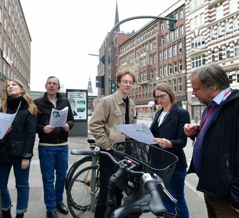Fünf Menschen stehen in der Innenstadt Hamburgs und schauen auf Zettel. 