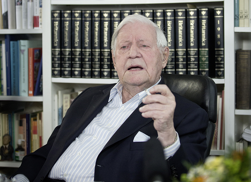 Altkanzler Helmut Schmidt sitzt mit Zigarette in der Hand vor Bücherregal.