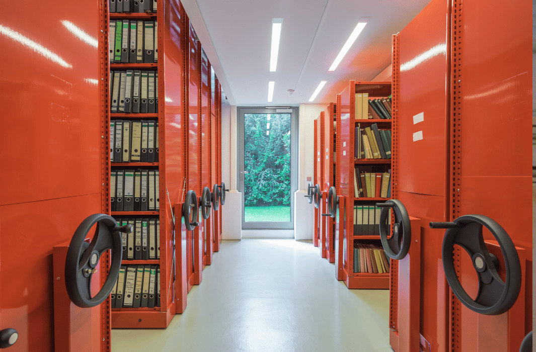 Rote Archivschränke mit Akten stehen in einem hellen Raum.