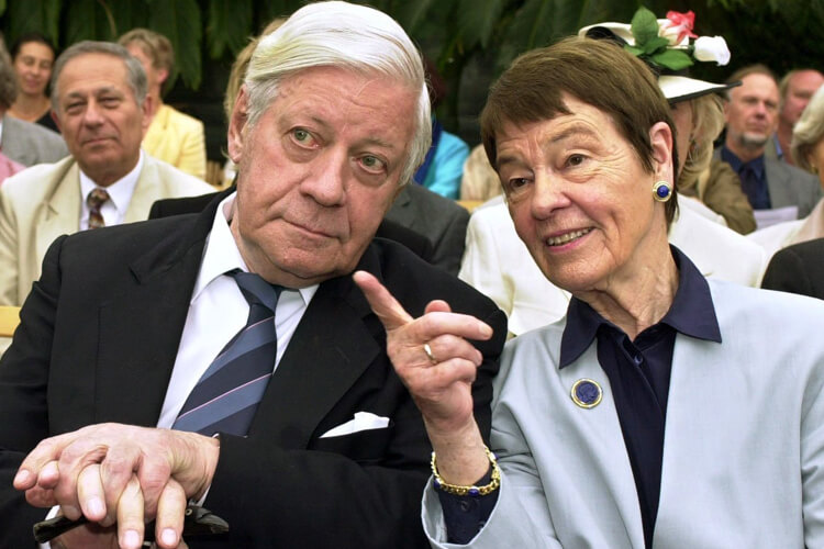 Helmut Schmidt lehnt sich zu Ehefrau Loki, die mit dem Zeigefinger auf etwas deutet.