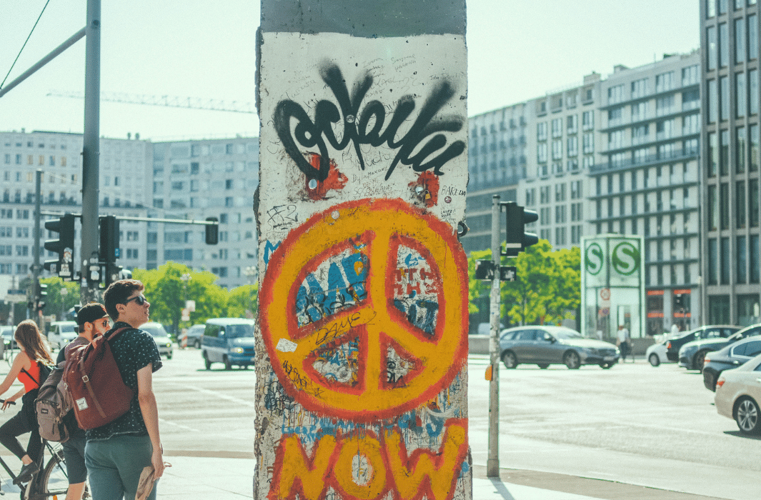Säule auf dem ein Graffiti zu sehen ist, das ein orangenes Peace-Symbol zeigt. 