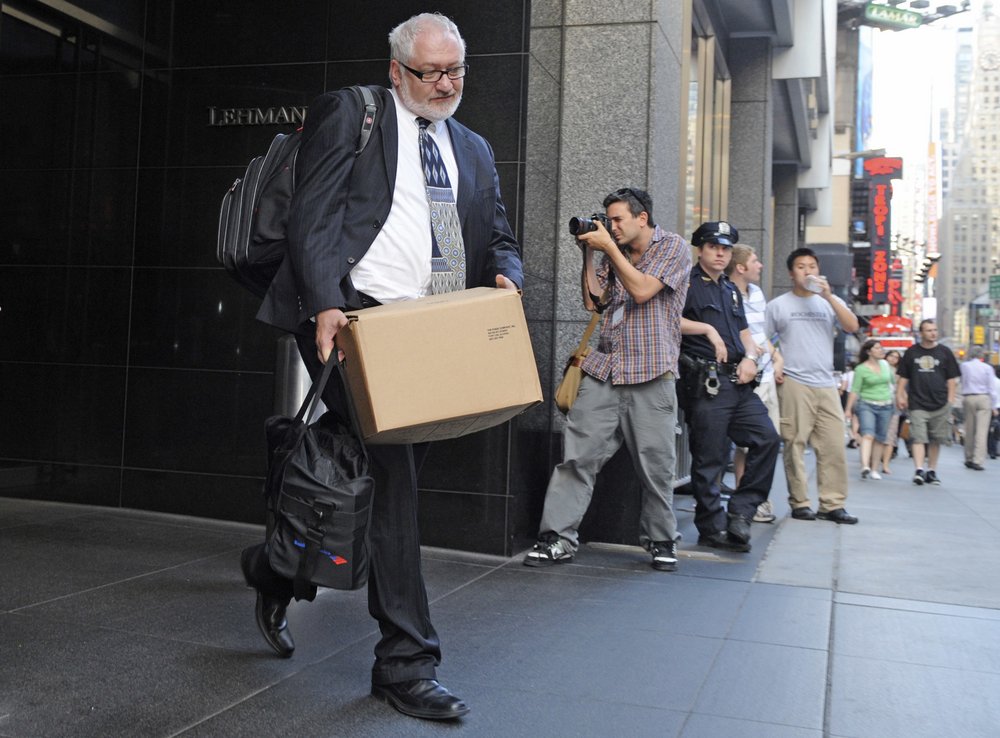 Man in a suit with a cardboard box in his hand on Wall Street, photographer and policewoman in the background