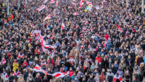 Crowd at demonstration with numerous white-red-white flags 