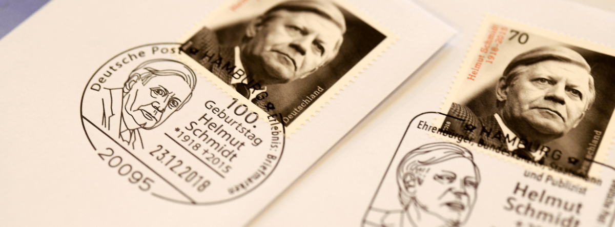 Großaufnahme einer Briefmarke mit einem Schwarz-Weiß-Porträt Schmidts und ein Stempelabdruck, der die Gesichtszüge von Helmut Schmidt abbildet.