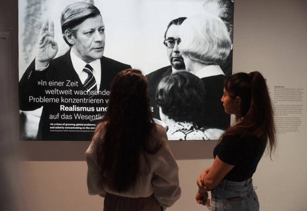 Zwei junge Frauen stehen vor einer Ausstellungstafel, auf der Helmut Schmidt zu sehen ist.