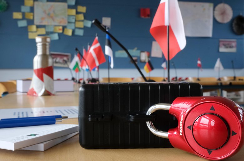 Colour photo: The setup for the escape game. A locked suitcase on a table, with flags of European countries in the background
