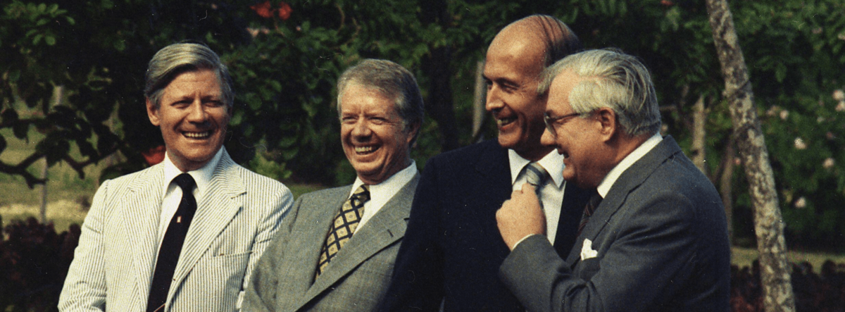 Die vier Männer stehen in Anzug und Krawatte nebeneinander und lachen.