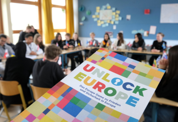 Der Flyer von "Unlock Europe" im Vordergrund. Die spielende Schulklasse des Helmut-Schmidt-Gymnasiums im Hintergrund.