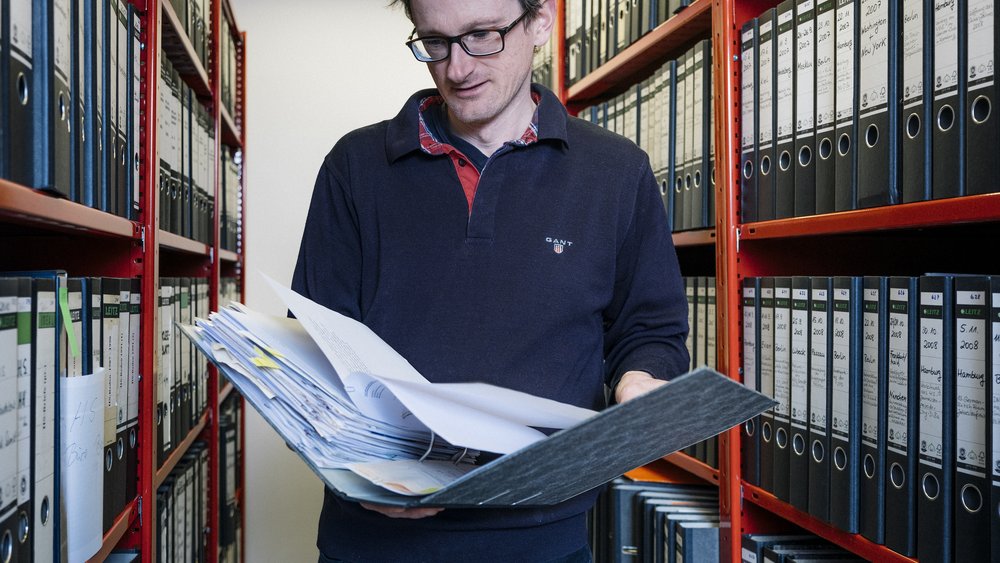 Man steht mit Zeitung in der Hand vor Archivschränken