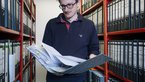 Man steht mit Zeitung in der Hand vor Archivschränken