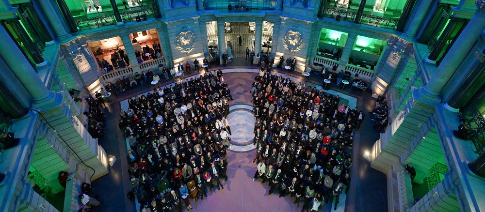 Colour photo: Looking from above, large room filled with people. Green lights.