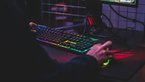 Person from behind, sitting in front of PC and colourful keyboard while gaming