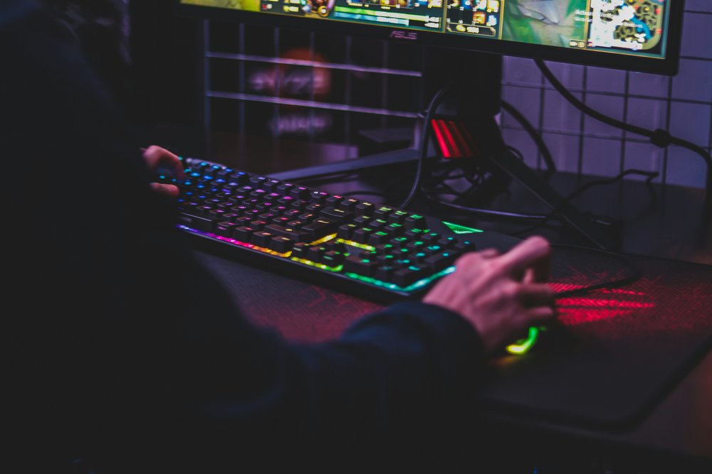Person from behind, sitting in front of PC and colourful keyboard while gaming