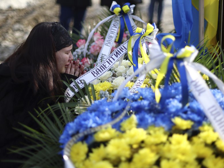 A woman mourns in front of a wreath of flowers with the colours of the Ukrainian flag