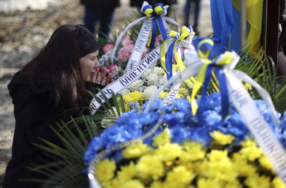 A woman mourns in front of a wreath of flowers with the colours of the Ukrainian flag