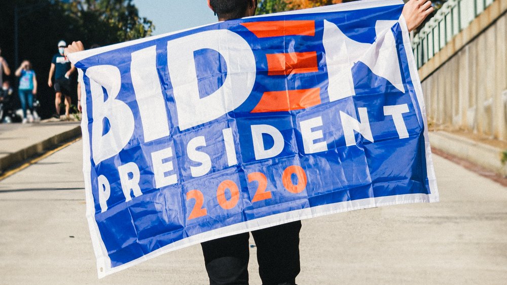 Man from behind with "Biden President" flag over his back