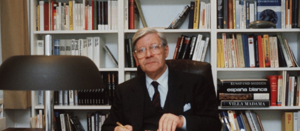 Helmut Schmidt an Schreibtisch sitzend vor Wandschrank mit Büchern