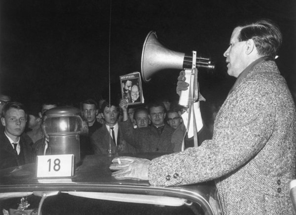 Helmut Schmidt steht umgeben von Demonstrierenden an einem Auto und spricht in ein Megaphon. Ein Demonstrant hält eine Ausgabe des Spiegels hoch.