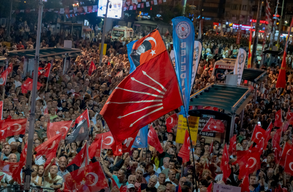 A crowd of people at a political rally with many Turkish flags and red party flags waving above the crowd