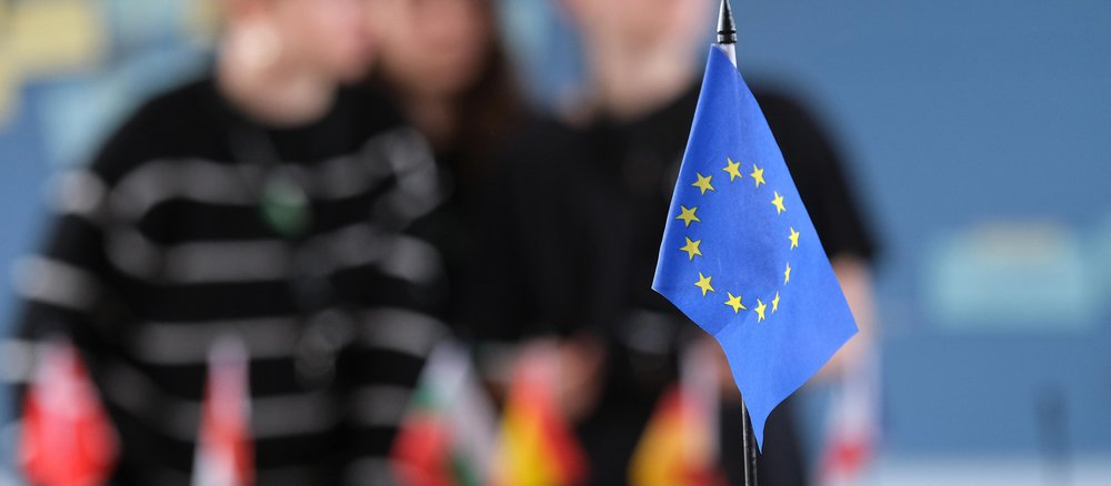 EU Flagge im Vordergrund und Schüler*innen verschwommen im Hintergrund