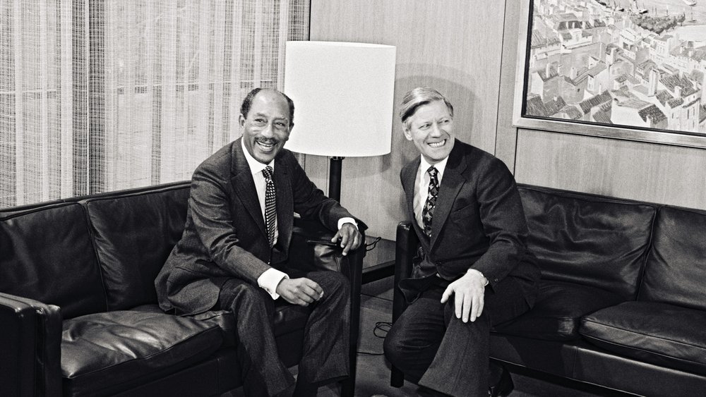 Helmut Schmidt and Anwar as-Sadat sitting on a couch and laughing