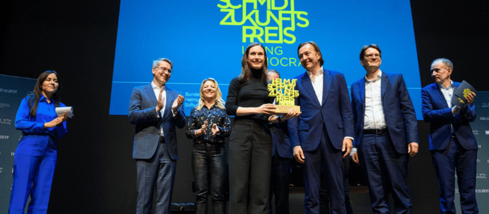 [Translate to English:] Sanna Marin gemeinsam mit den Jurymitgliedern und Aline Abboud auf Bühne mit Preis in Hand.