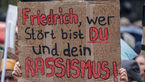 Demonstrationsschild mit Aufschrift "Friedrich, wer stört bist du und dein Rassismus!"