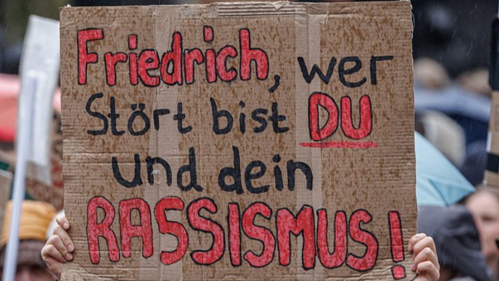 Demonstrationsschild mit Aufschrift "Friedrich, wer stört bist du und dein Rassismus!"