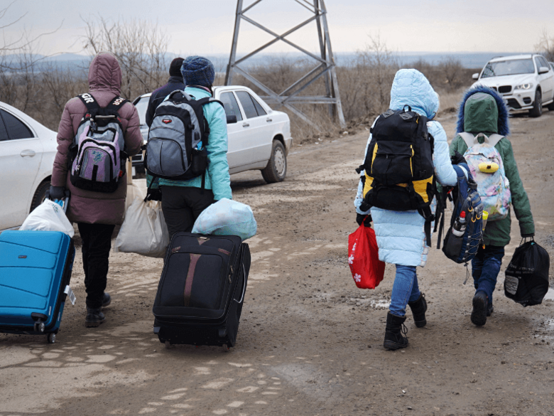 Ukrainian refugees with suitcases and rucksacks from behind