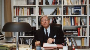 Helmut Schmidt sitting at a desk in front of a wall cupboard with books