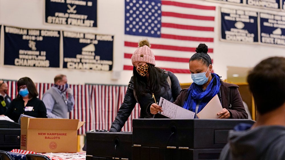 Wahllokal in Amerika, Personen mit Atemschutzmasken stehen an Wahlurnen