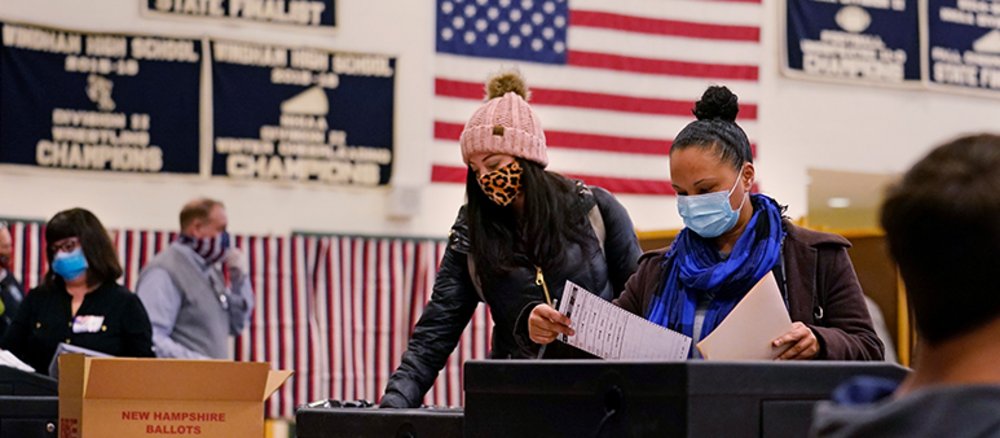 Wahllokal in Amerika, Personen mit Atemschutzmasken stehen an Wahlurnen