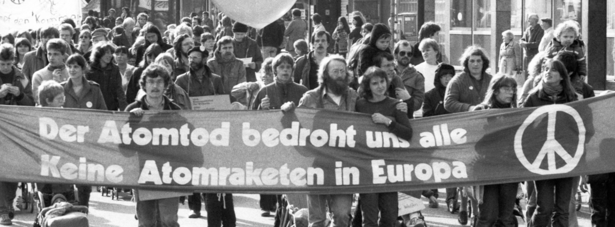Historisches Foto von Demonstrierenden. Auf einem großen Banner steht "Der Atomtod bedroht und alle - Keine Atomraketen in Europa"