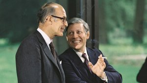 Farbfoto 1977: Helmut Schmidt lächelt im Gespräch mit einem Mann im Nadelstreifenanzug; in der Hand hält Schmidt eine Zigarette.