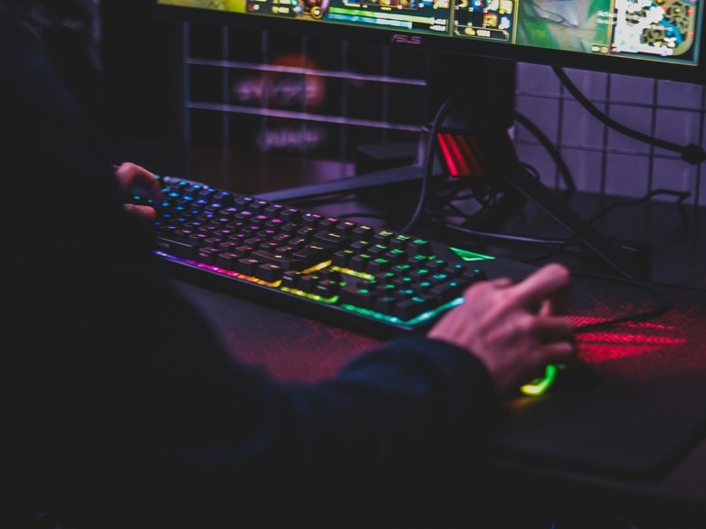 Person from behind, sitting in front of PC and colourful keyboard while gaming