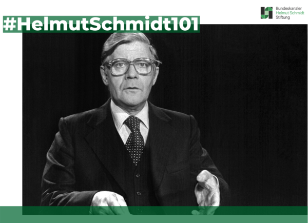 Helmut Schmidt speaks in front of a Camera in a studio. He wears a dark suit and large glasses. 