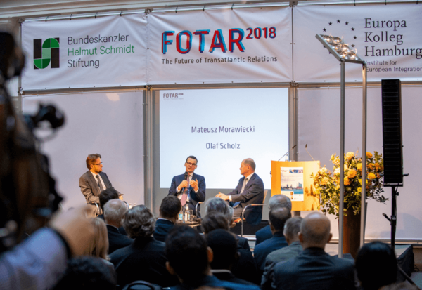 Drei Männer führen ein Gespräch auf einer Bühne. Über ihnen ist ein Banner mit den Logos der Bundeskanzler Helmut-Schmidt-Stiftung, der FOTAR 2018 und des Europa Kolleg Hamburg.
