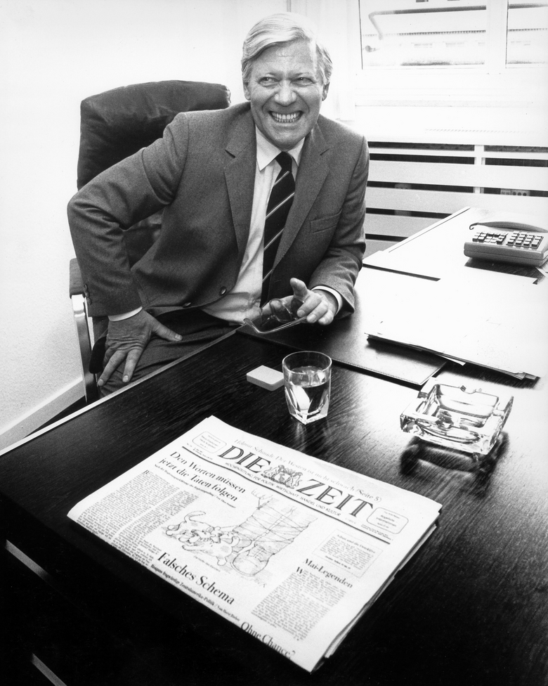 Black-and-white photograph of Helmut Schmidt sitting at his desk and laughing